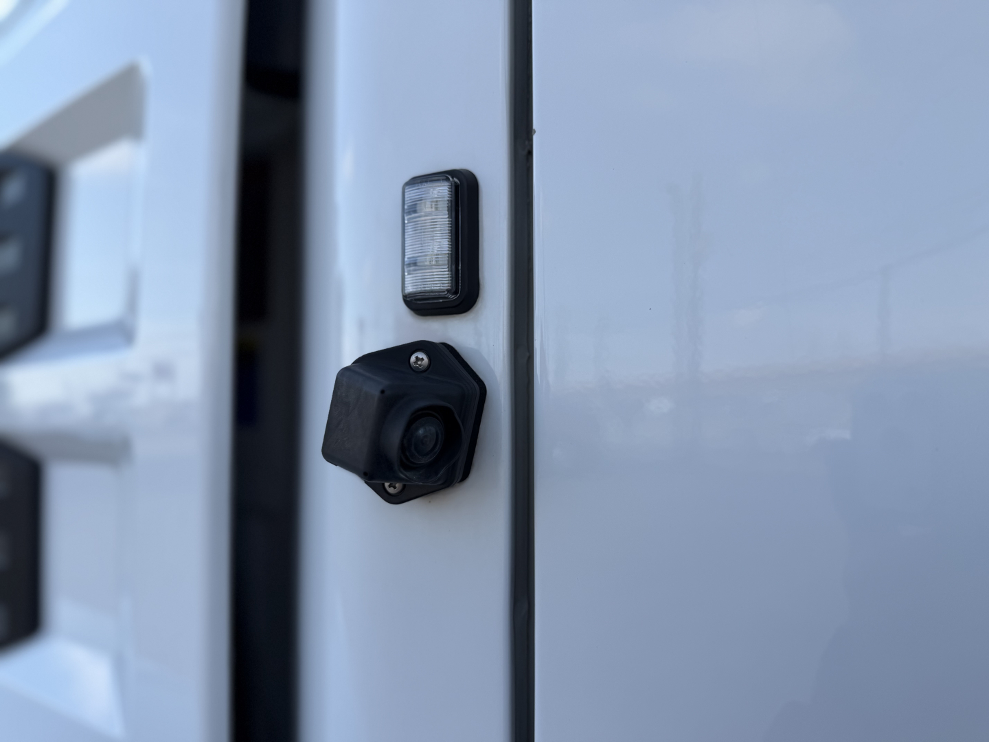 Close-up of a side mirror or camera housing area on a 2023 Mack ANTHEM 64T showing a small rectangular light and a black circular camera/sensor fitted on the door frame.