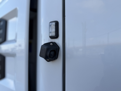 Close-up of a side mirror or camera housing area on a 2023 Mack ANTHEM 64T showing a small rectangular light and a black circular camera/sensor fitted on the door frame.