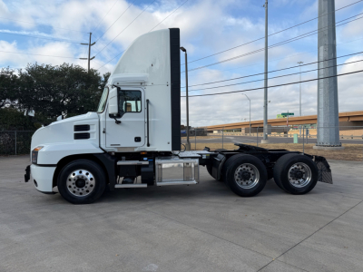 Truck side view of a white 2023 Mack ANTHEM 64T highway tractor with sleeper cab, tag axle, and five-wheel configuration. Visible are fuel tanks, steps, and exhaust stacks.