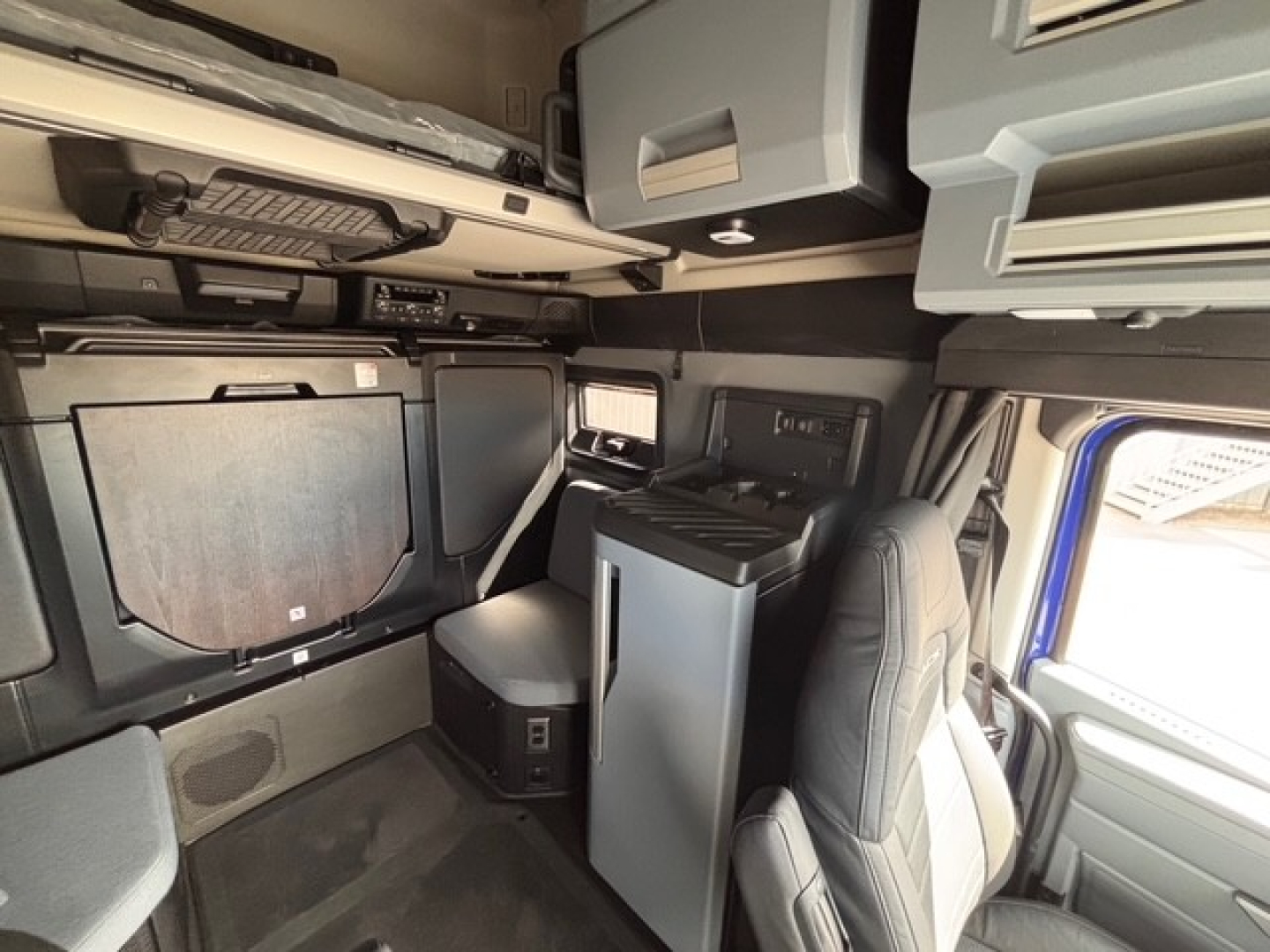 Truck cab interior showing sleeper area with overhead storage, cabinets, and driver seat in Mack PR64T76H interior.