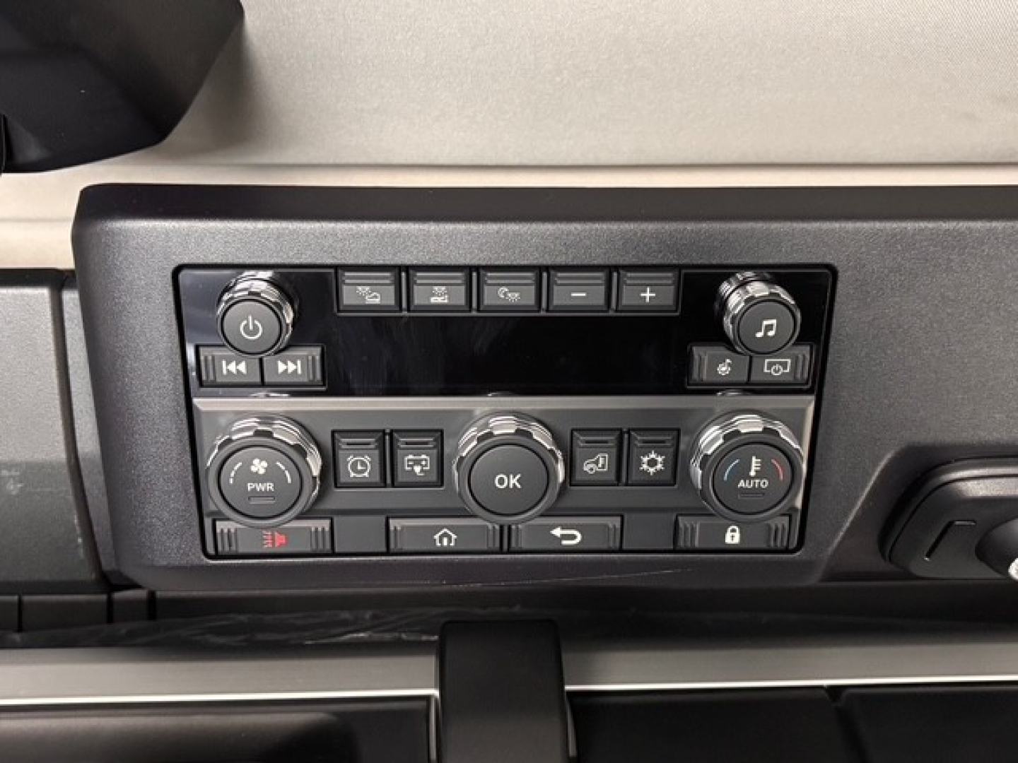 Dashboard control panel in a Mack truck with multiple buttons and dials, including volume knob, climate controls, and indicator lights.