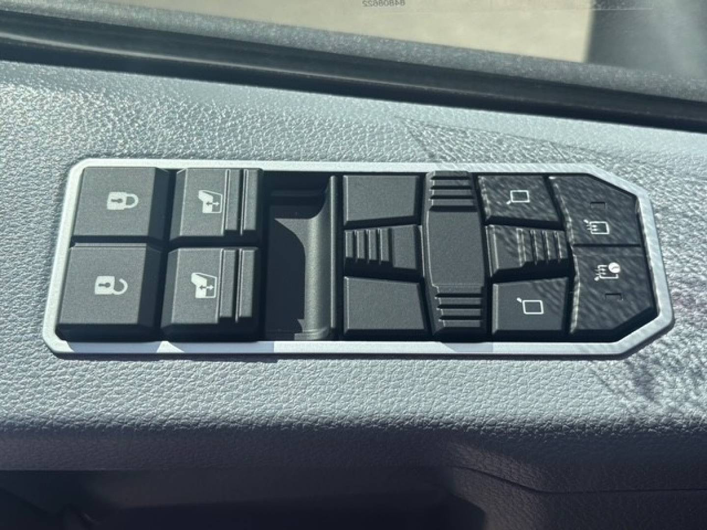 Vehicle window/door controls panel: four window switch buttons, lock button, mirror adjustment pad, and memory/lock icons visible.