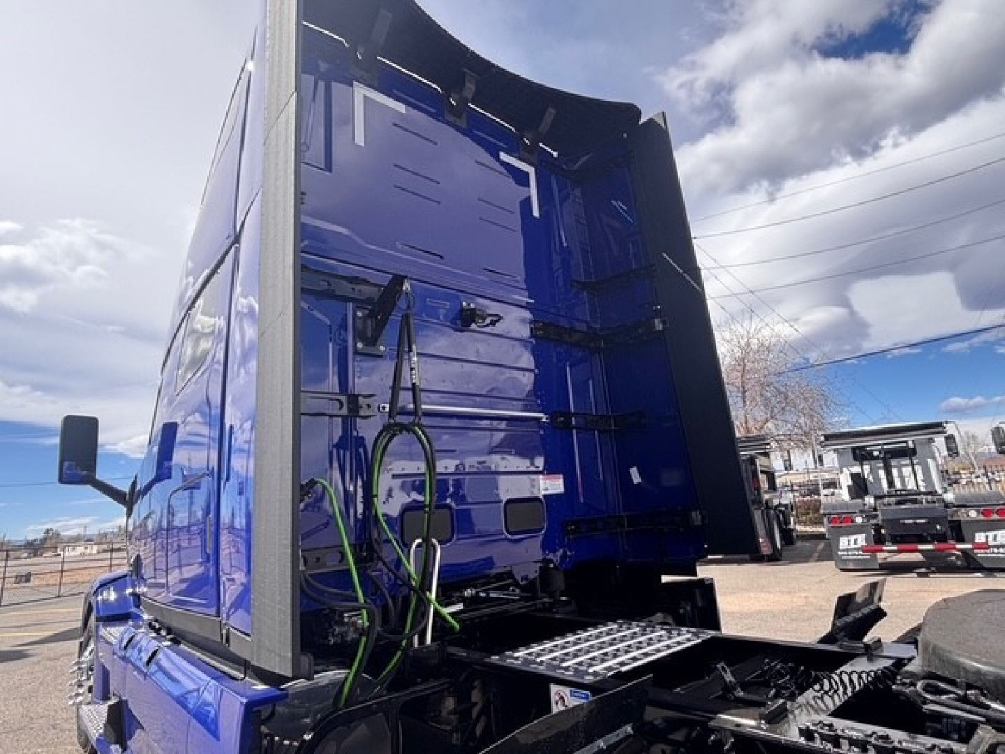 Truck cab rear interior view of a blue Mack PR64T76H with cargo area open, showing wiring harnesses and rear frame.