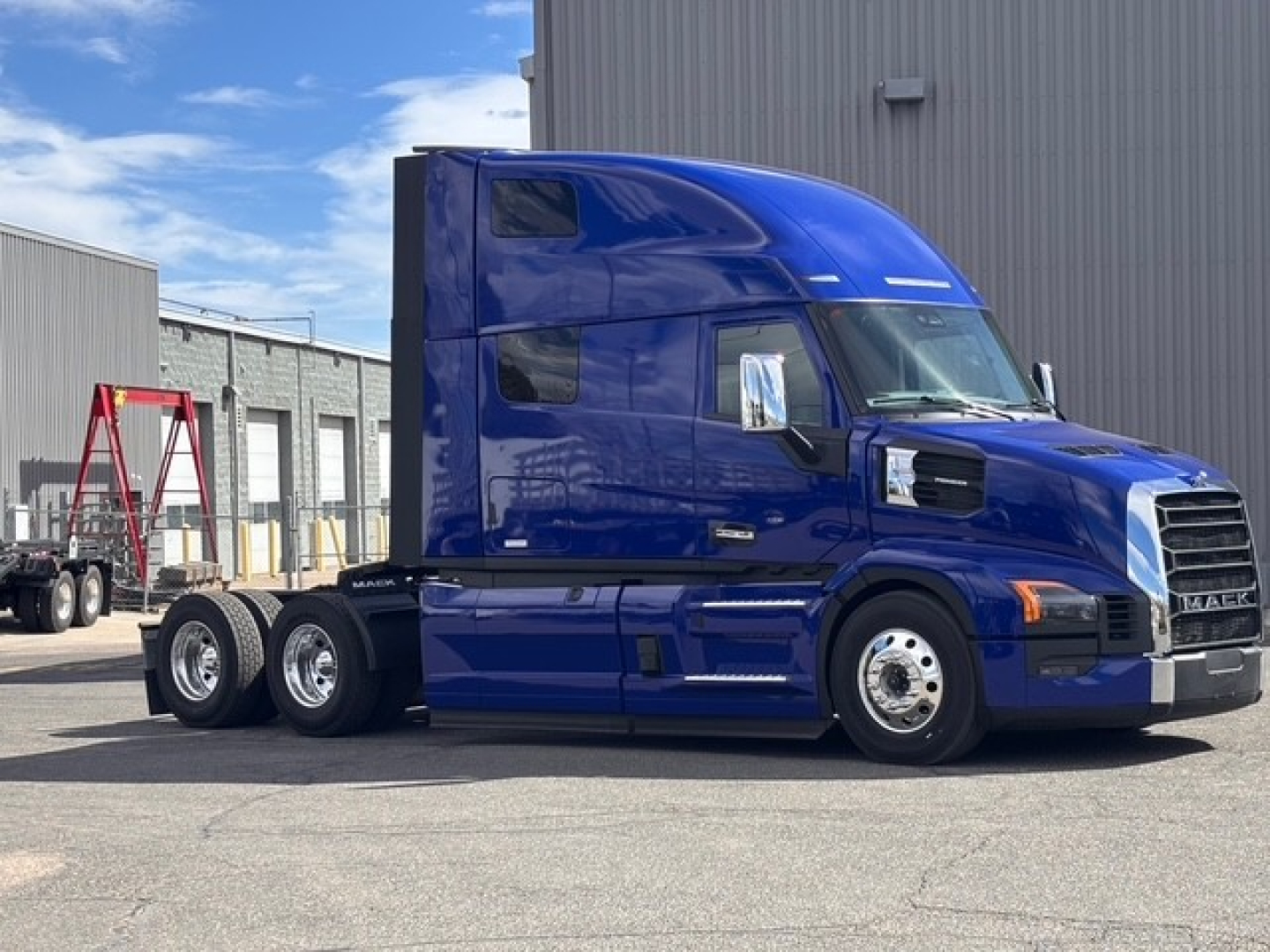 Blue Mack PR64T76H truck tractor with sleeper cab, side view showing chrome fuel tanks and dual rear axles on a dealership lot.