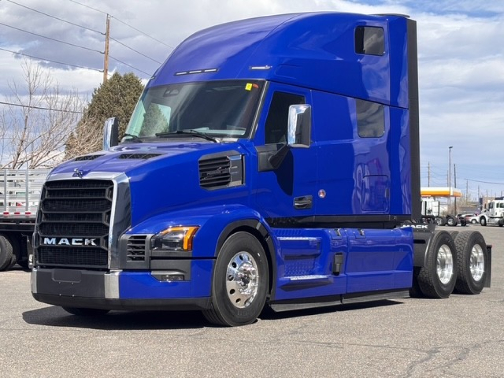 Blue Mack truck in profile view, front grille shows MACK branding; side shows V-closer cab with sleeper, chrome mirrors, dual rear axles; windows with tinted glass.