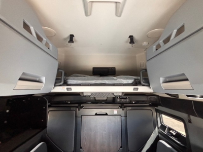 Cab interior of a new Mack PR64T76H sleeper tractor showing bunk area and storage compartments.