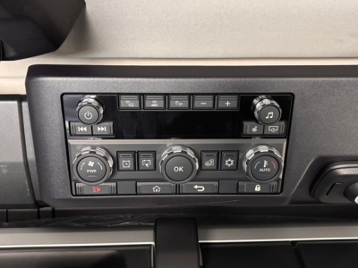 Dashboard control panel in a Mack truck with multiple buttons and dials, including volume knob, climate controls, and indicator lights.