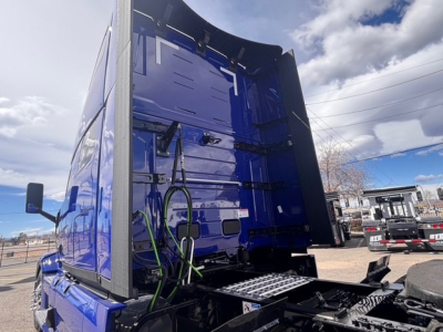 Truck cab rear interior view of a blue Mack PR64T76H with cargo area open, showing wiring harnesses and rear frame.