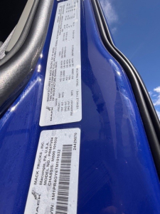 Mack truck VIN label and information plate on blue exterior showing model details and serial numbers.