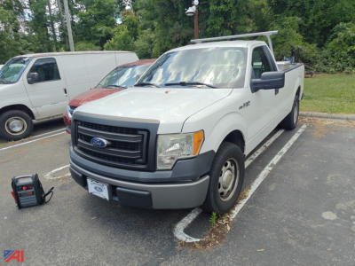 Ford F-150 pickup truck in a parking lot showing front grille and side mirror with tool chest nearby.