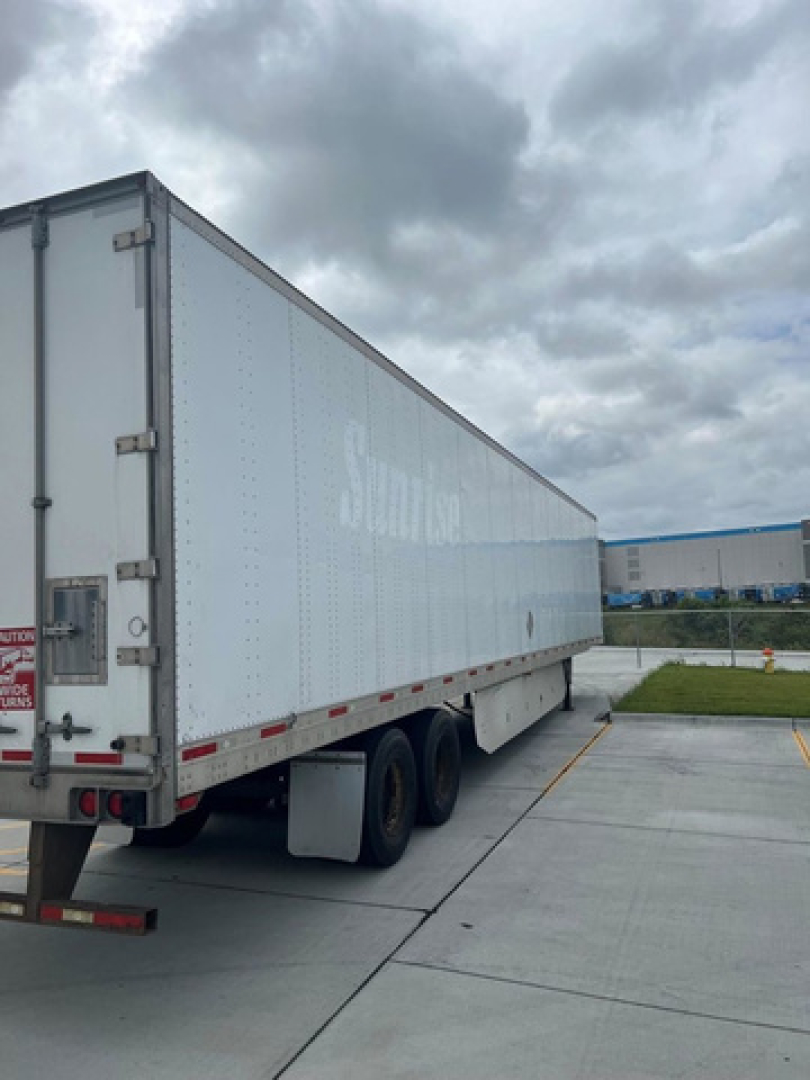 Trailer side view of a white utility van trailer with tandem axles.
