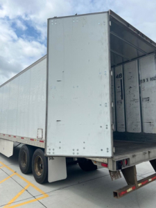 Utility van trailer interior showing open rear cargo door and empty aluminum trailer with wheels and ramp.