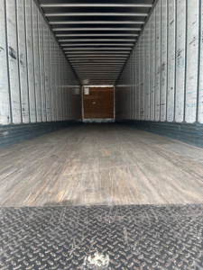 Empty Utility van trailer interior with wood floor and metal walls, rear doors, no visible labels or numbers.