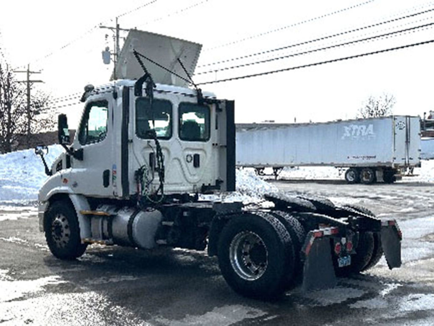 Truck cab rear showing Freightliner Cascadia chassis with fifth wheel removed, exposed frame and rear wheels, and a snow-covered lot.