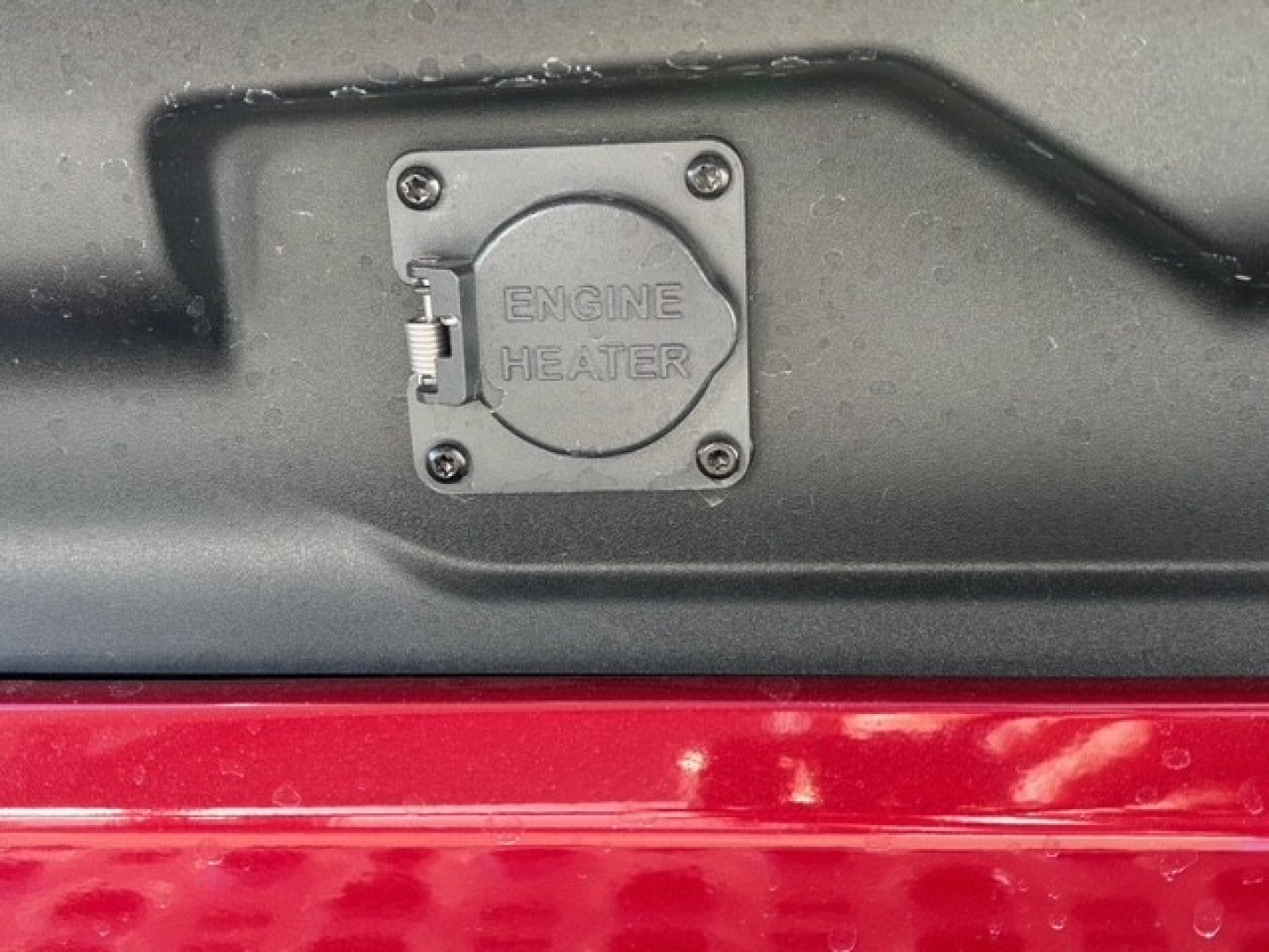 Engine heater cap and surrounding area on a Mack truck, with a visible round engine heater cap and screws.