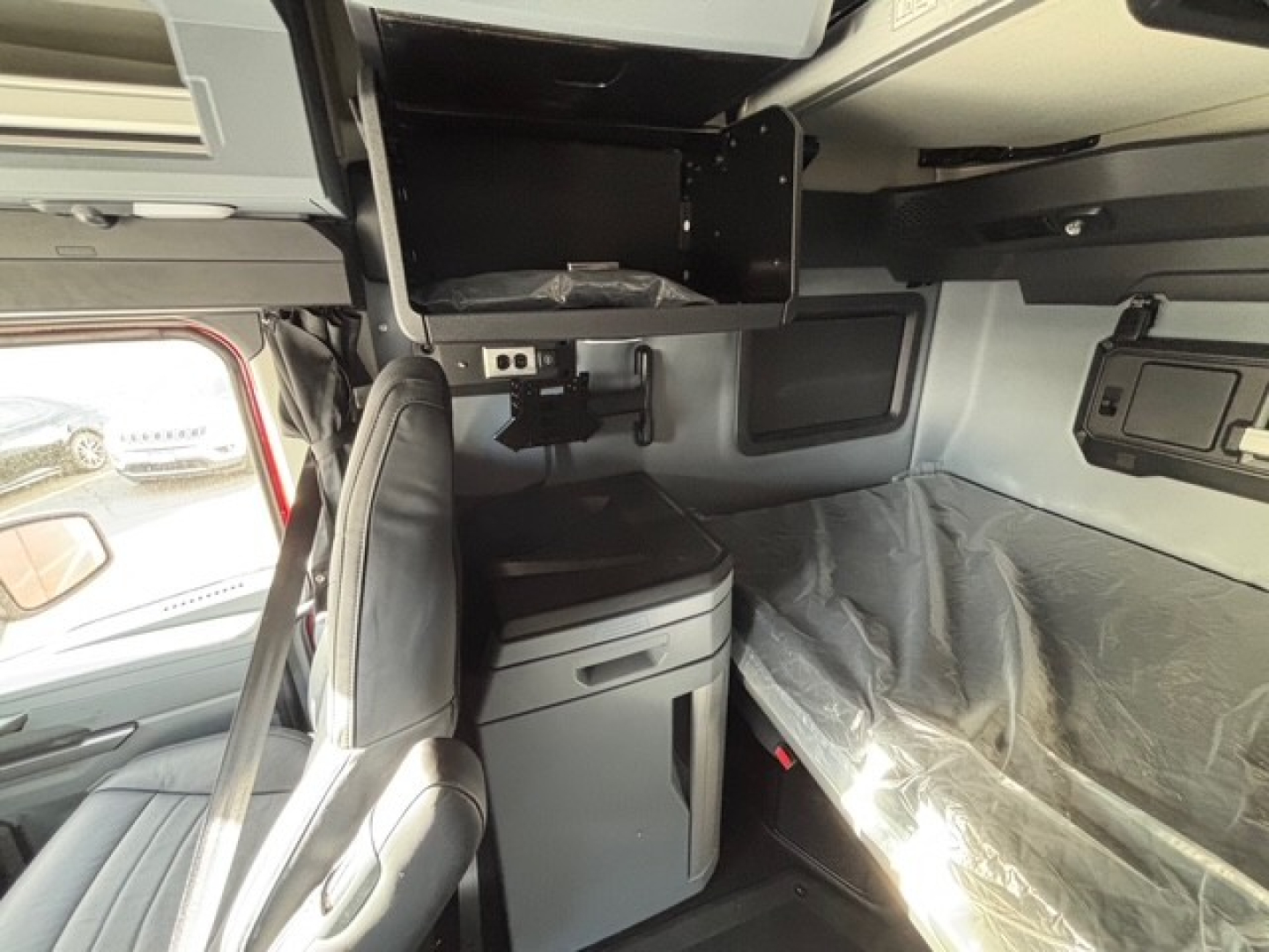 Cab interior of a new Mack PR64T76H sleeper truck showing dashboard, overhead storage, and sleeping area with plastic cover.