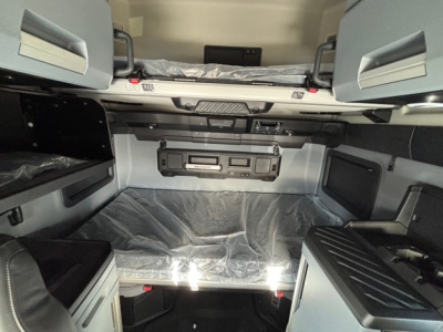 Cab interior of a new Mack PR64T76H sleeper showing overhead storage shelves and control panel with text visible.