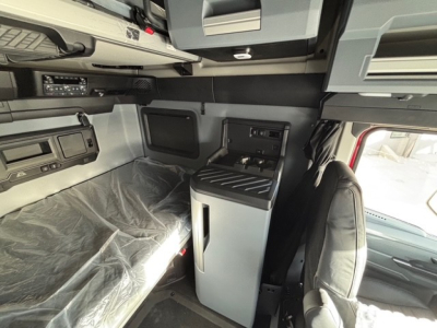 Interior of a new 2026 Mack PR64T76H truck cab with sleeper area, showing bunk bed area covered in plastic, overhead storage, and a center console with controls.
