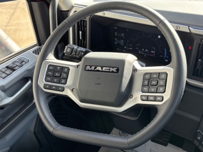 Steering wheel in Mack PR64T76H cabin with Maek emblem and control buttons on both sides; dashboard display behind