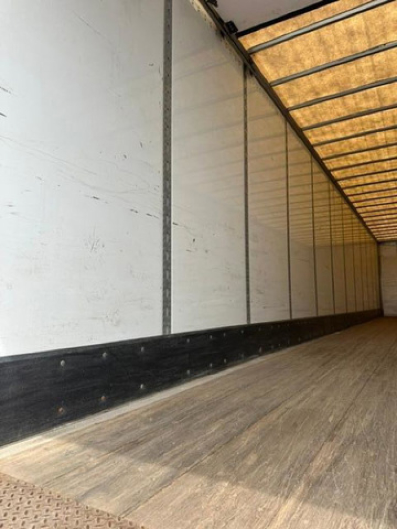 Interior side of a trailer with wooden floor and white walls, showing a long empty cargo area. There are no legible labels or text visible in the image.