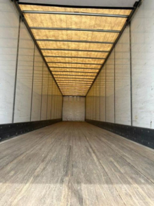 Trailer interior showing empty cargo area with wooden floor and white walls, long box trailer with overhead roof panels.