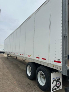 Trailer side view showing white Wabash van trailer with dual rear axles and reflective tape.