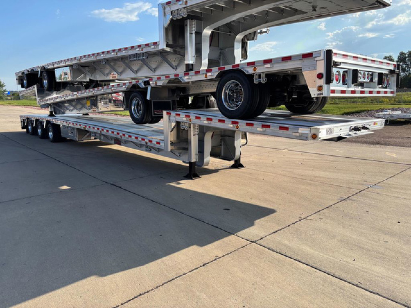 Trailer landing gear supported dropdeck trailer with multiple axles and a folded deck. Visible markings include reflective tape and wheels.