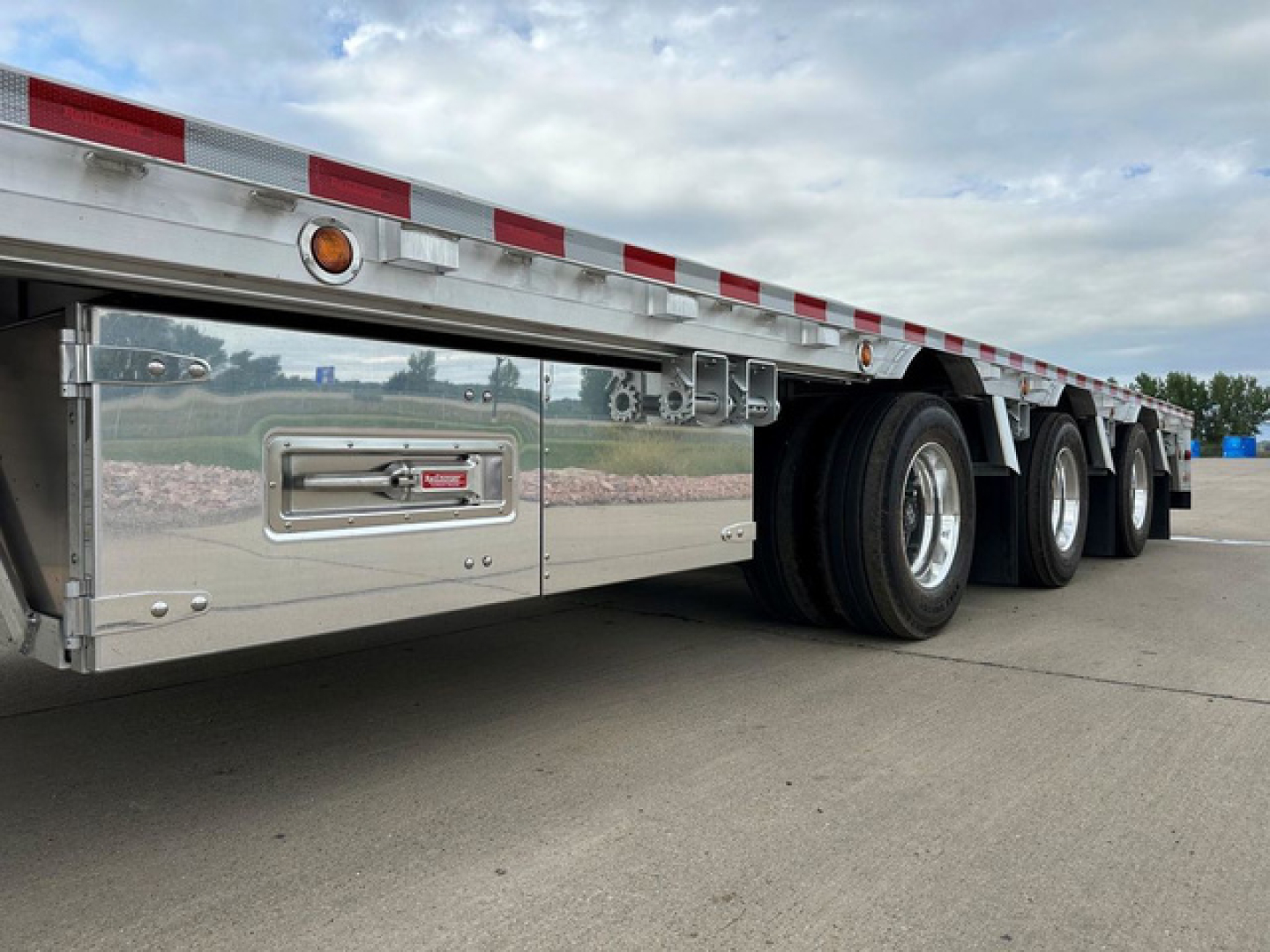 Dropdeck trailer side view showing aluminum side panels, dual wheels, and underbody toolbox with Reitnouer logo.
