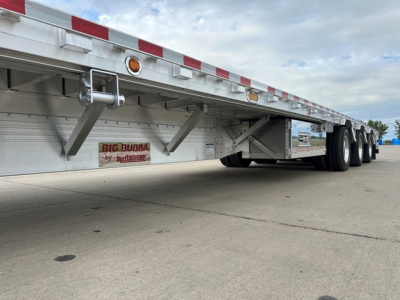 Trailer underside showing landing gear housing and dual rear axles, with a small sticker reading 'BIG RUBBA by Reitnouer' on the side.