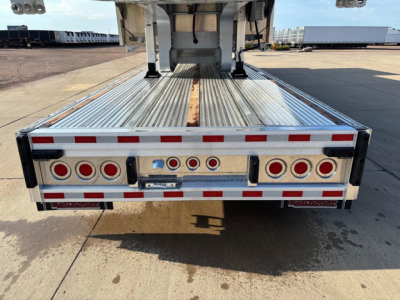 Trailer rear view showing dropdeck configuration with bumper and multiple round tail lights, reflective tape, and metal deck surface.