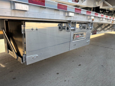 Dropdeck trailer side with metal access panels and hinge details; visible are bolted box compartments and a small label area.