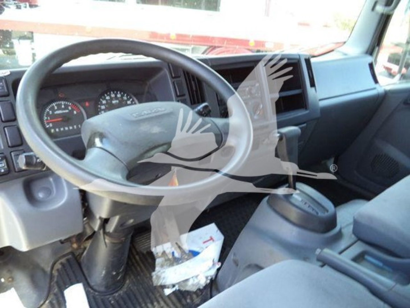 Isuzu NPR cargo truck cab interior showing steering wheel, dashboard gauges, and center console with cup holder and papers.