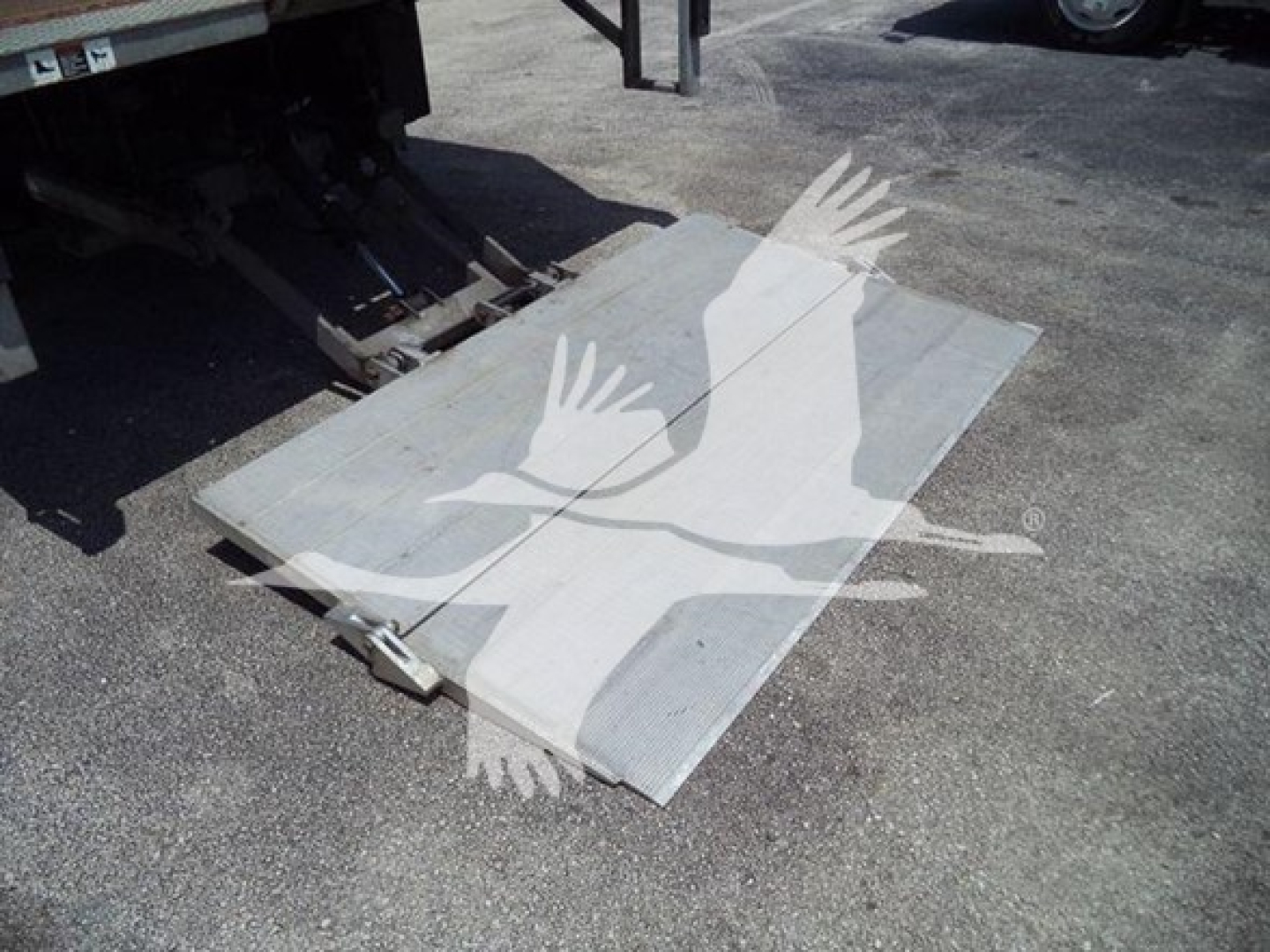 Isuzu NPR truck bed ramp/plate with metallic surface and hinge hardware, docked near a truck tailgate.