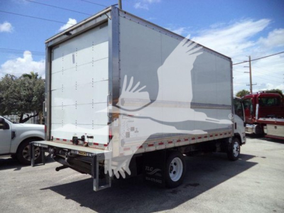 Isuzu NPR box truck rear/side view showing cargo box, white panels, rear liftgate, dual rear wheels, and safety decals.