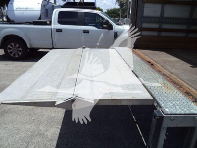 Isuzu NPR truck with a flatbed/towbed in a lot showing a metal platform and vehicle in background.