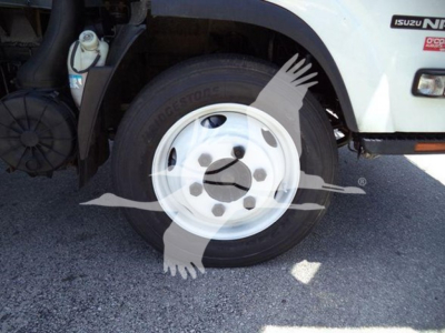 Isuzu NPR truck front wheel well and tire showing Bridgestone tire, white steel wheel, part of box truck body with Isuzu badge visible