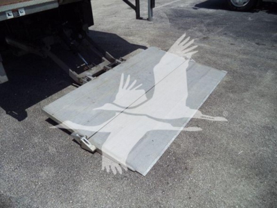 Isuzu NPR truck bed ramp/plate with metallic surface and hinge hardware, docked near a truck tailgate.