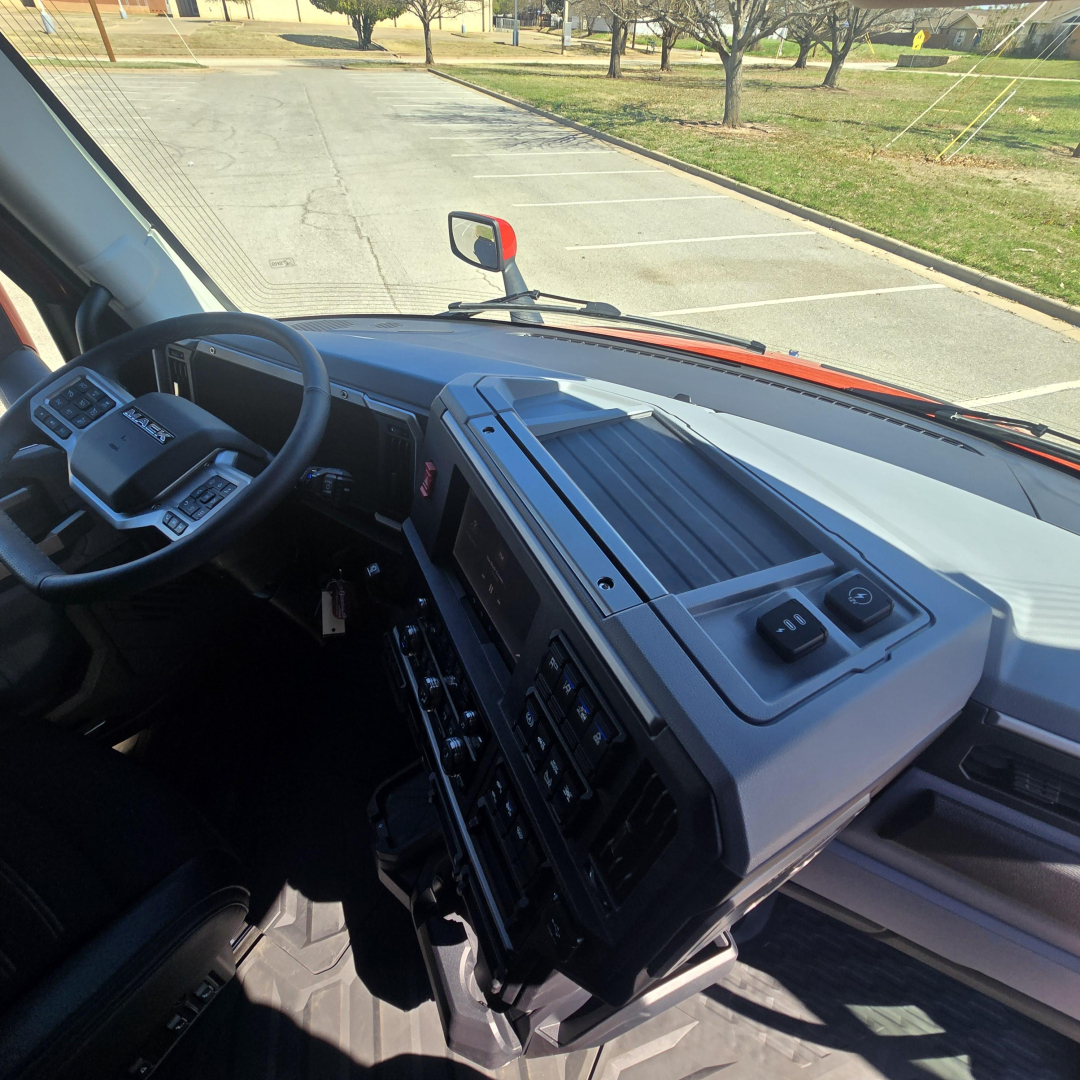 Truck cab interior of a 2026 Mack PR64T76H showing the instrument panel, steering wheel, and dashboard from the passenger side.