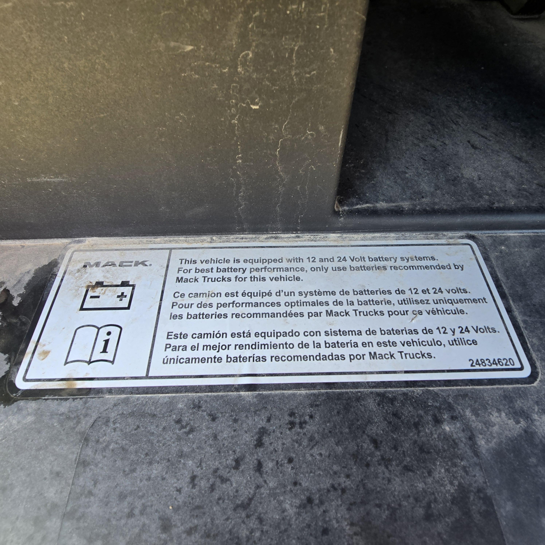 Label on Mack truck showing 12V/24V battery system and battery recommendations in English, French, and Spanish.