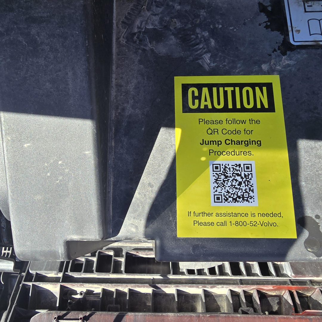 Caution label on Mack truck component showing QR code for jump charging procedures.