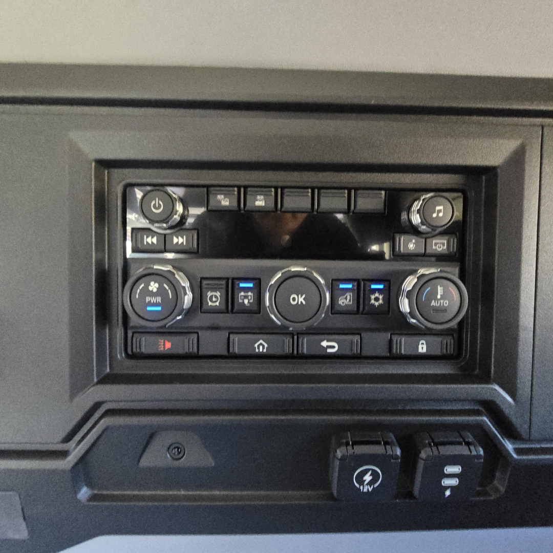 Truck cab interior control panel with multiple buttons and a center OK button, circular dials, and a USB-like port; no legible labels for specific model text visible.