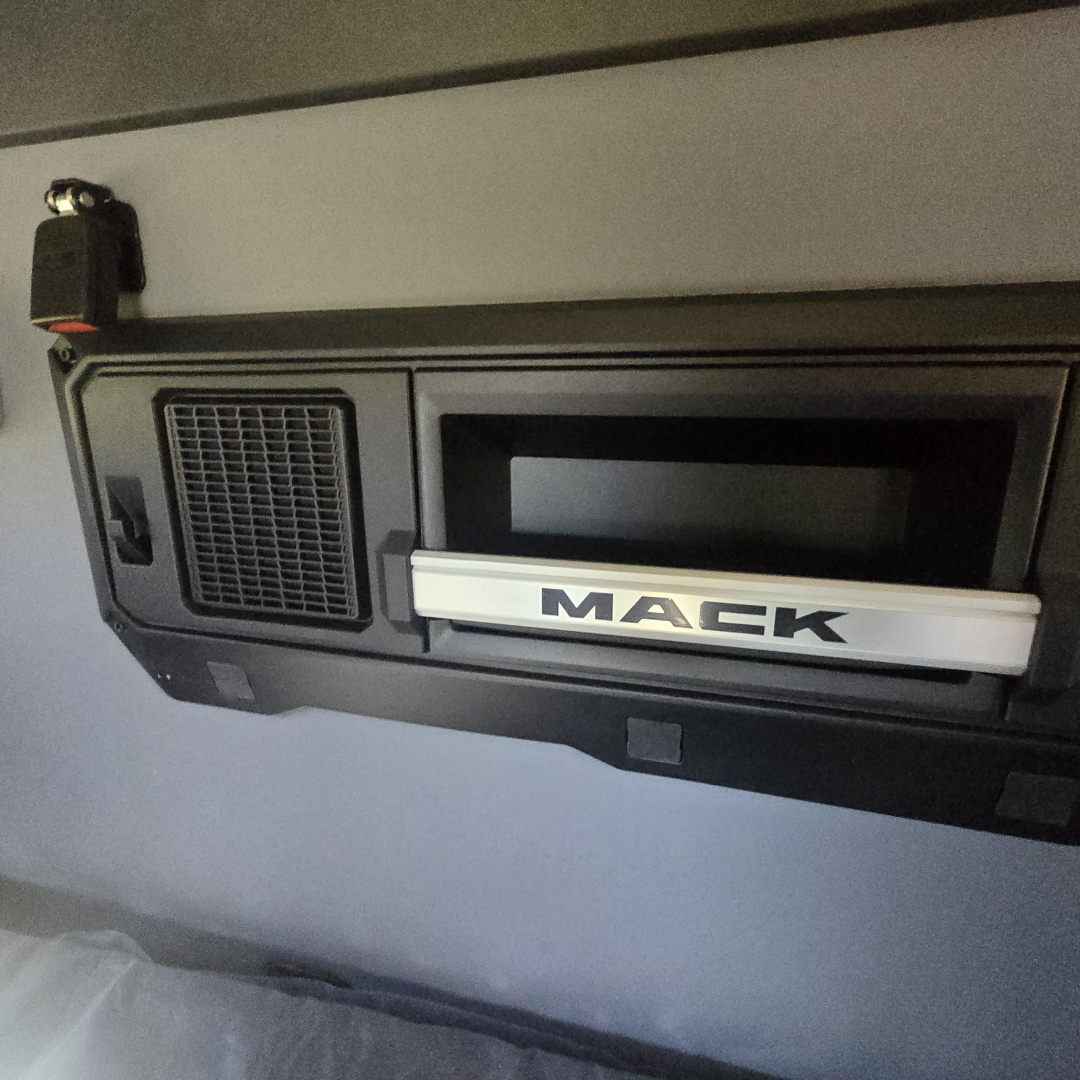 Mack PR64T76H dash area showing Mack badge and vent/controls in a truck cab.