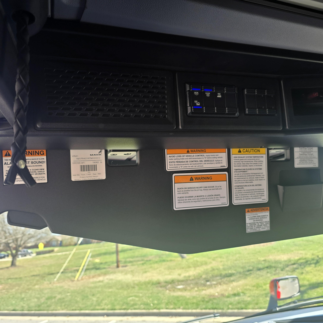 Dashboard area of a Mack PR64T76H truck showing warning labels and control panels on the lower dash