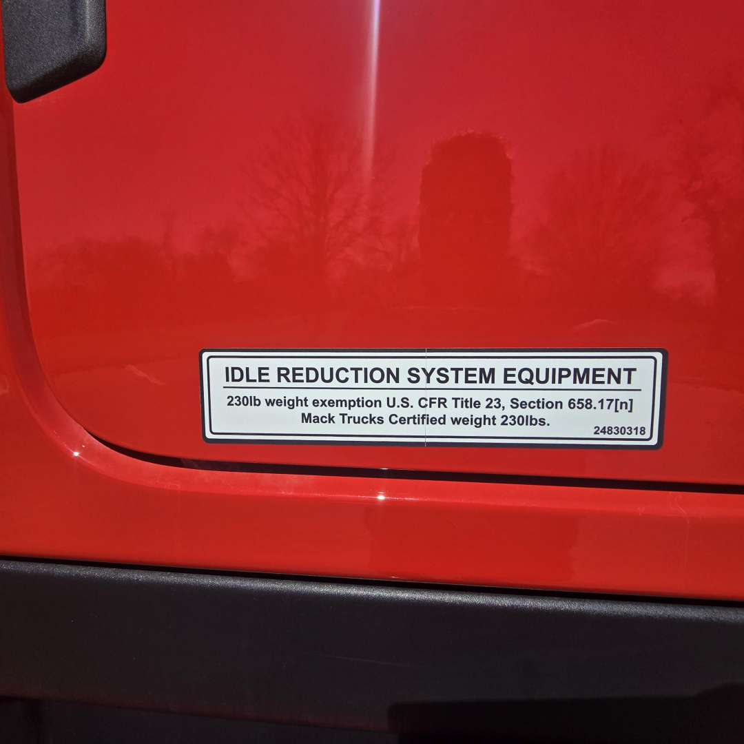 Mack PR64T76H idle reduction system equipment label on red truck cab showing 230lb weight exemption info and Mack Trucks certified weight 230lbs.