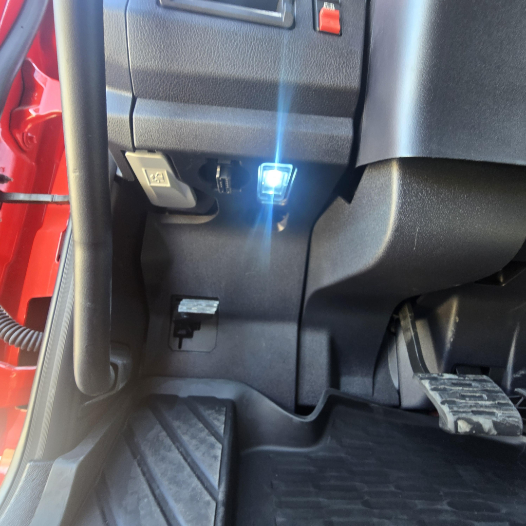 Cab interior footwell of a Mack PR64T76H showing a blue LED indicator near the driver area, pedals, and lower dashboard with plastic panels.