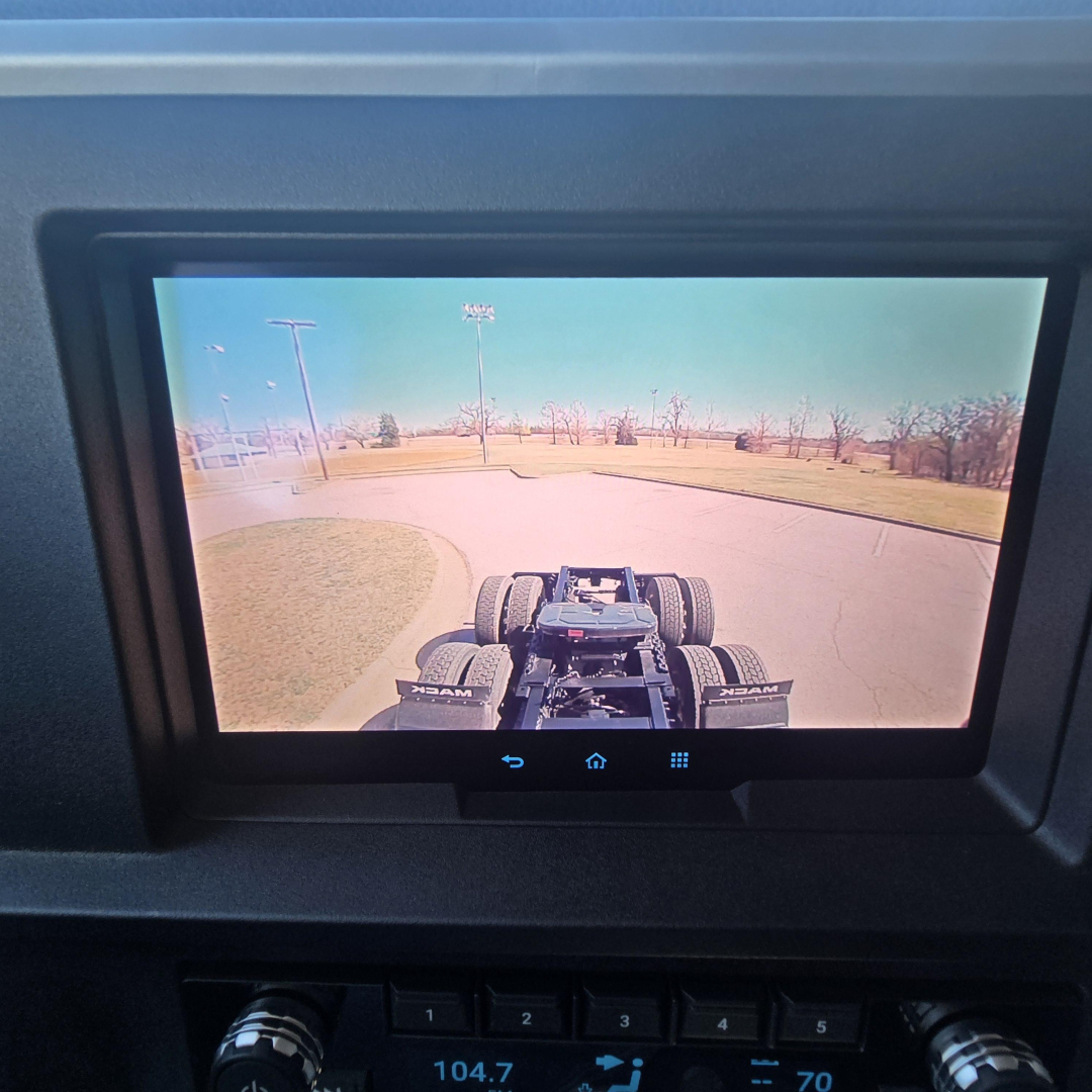Rear view camera display showing truck chassis and dual rear axles, with tire details and road in background.