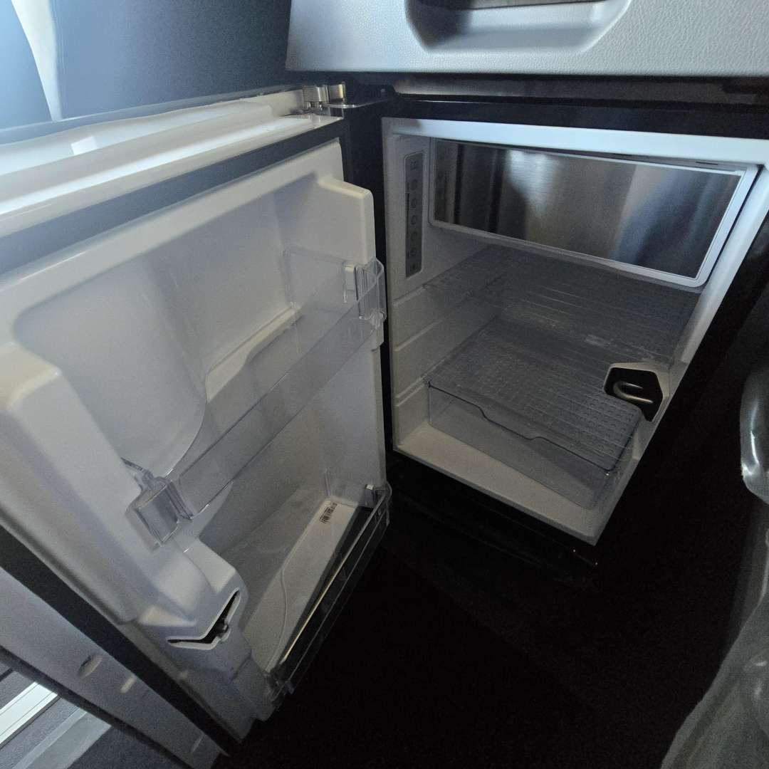 Refrigerator and compact freezer in a Mack PR64T76H truck cab showing open door compartments and interior shelves.