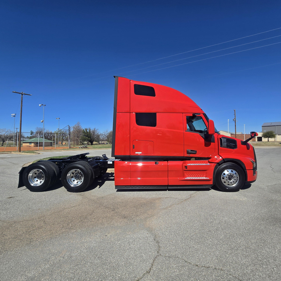 Semi truck tractor unit in red, side view showing sleeper cab and dual rear axles with fifth wheel, no trailer attached.