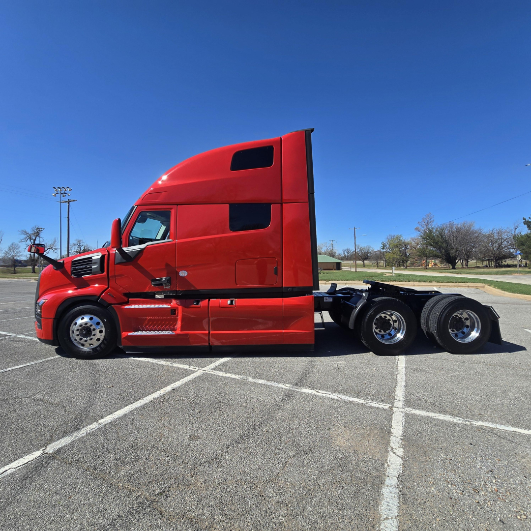 2006 Mack PR64T76H conventional sleeper truck tractor side view showing red cab and three rear axles with chrome wheels.