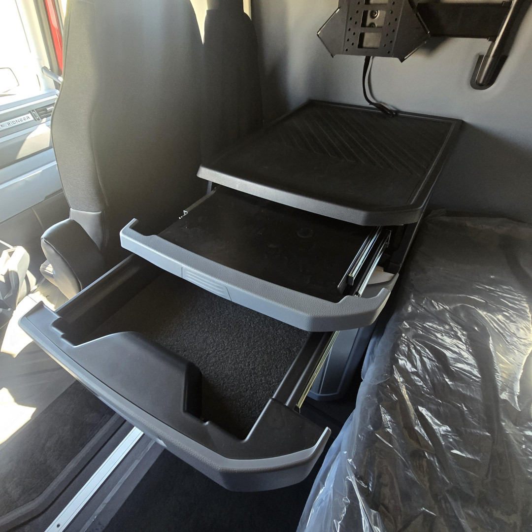 Cab interior showing open storage drawers in a new Mack PR64T76H truck sleeper with labeled compartments and a plastic organizer tray.